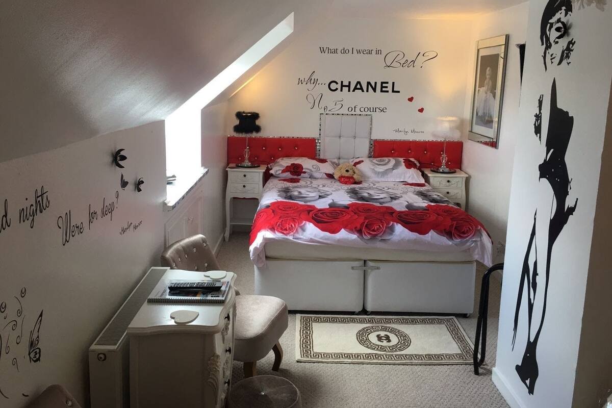 A bedroom with a bed, bedside tables, a desk, and a chair. There are wall decorations, including a quote and a silhouette.