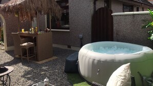 A cozy outdoor seating area with a thatched umbrella, a hot tub, and a stone wall. - Gleninver Guest House (Inverness)
