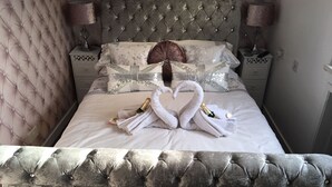 A bed with a tufted headboard, two bedside tables with lamps, and a decorative swan towel arrangement with champagne bottles. - Gleninver Guest House (Inverness)