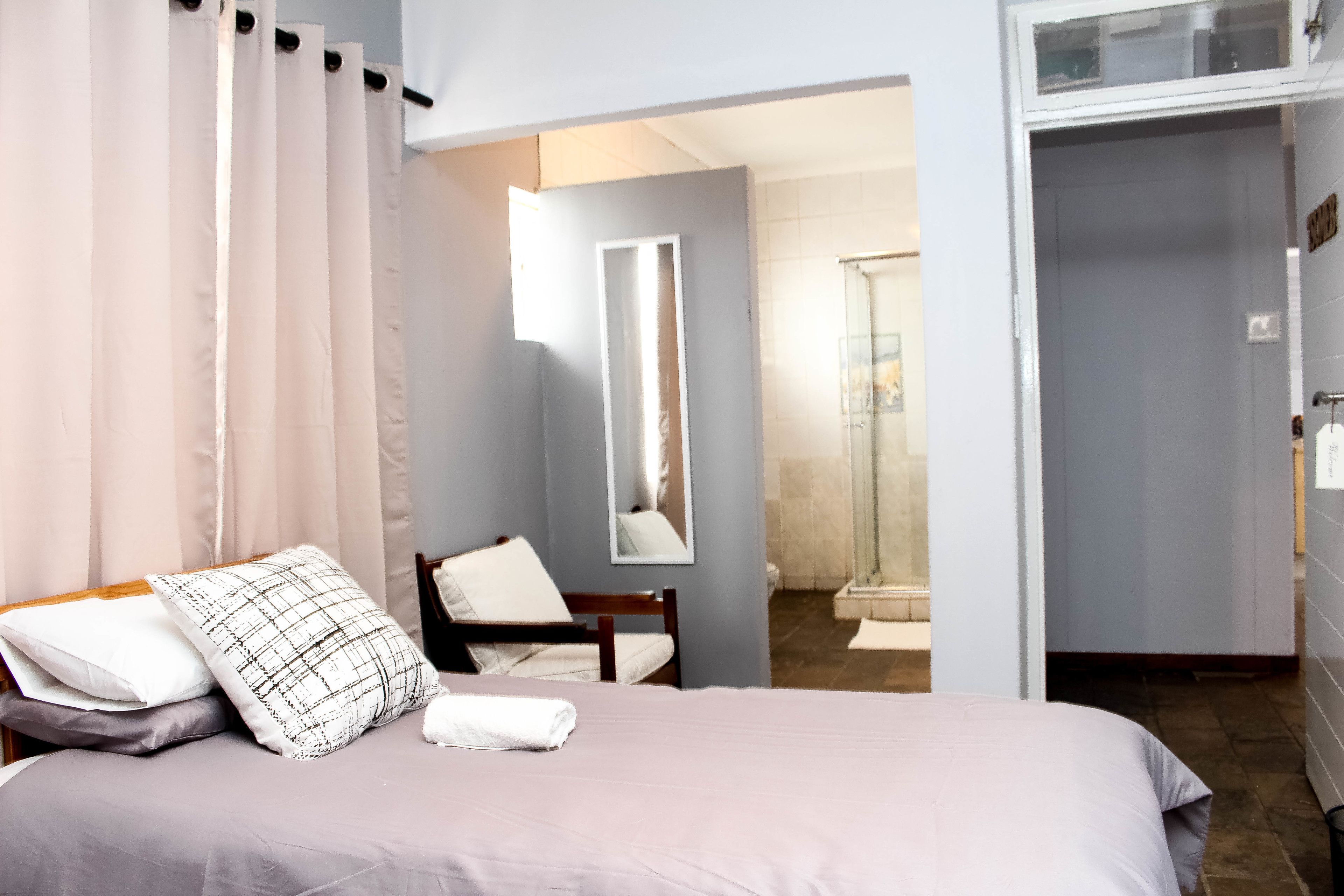 A hotel room with a bed, a chair, a mirror, and a bathroom visible through an open door.