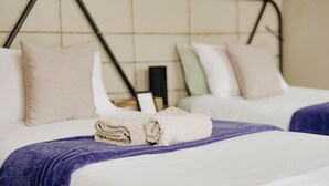 A hotel room with two beds, each with a rolled white towel and a purple blanket. - Kate's Nest Guesthouse (Windhoek)