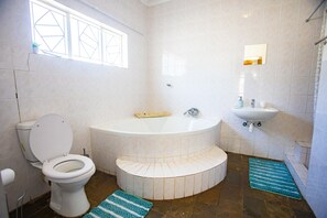 A bathroom with a toilet, a bathtub, a sink, and a window. - Kate's Nest Guesthouse (Windhoek)