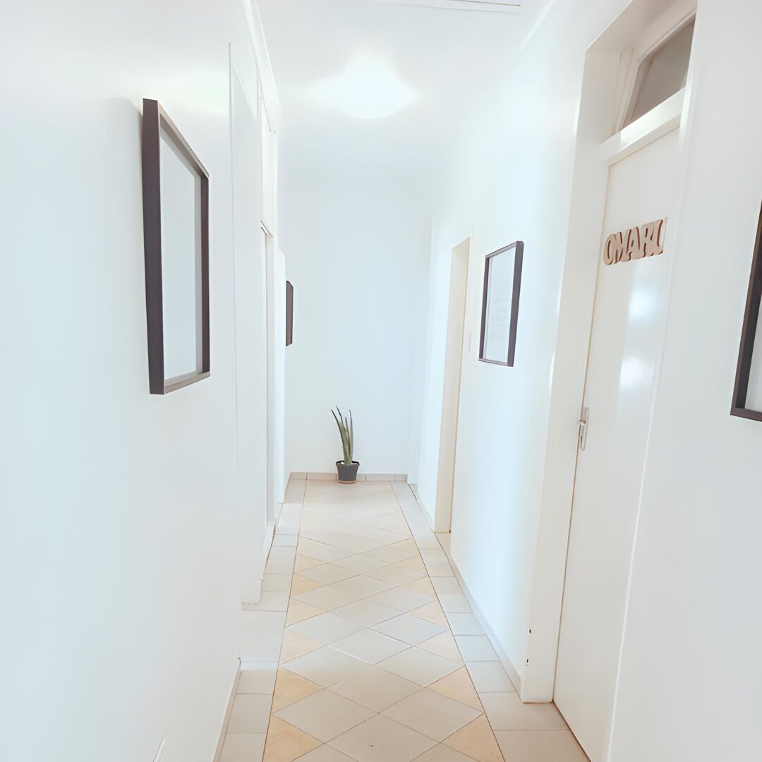 A hallway with white walls, framed pictures, and a potted plant.