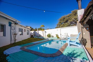 A swimming pool with a tiled deck, a white fence, and a blue chair. - Kate's Nest Guesthouse (Windhoek)