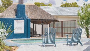 A pool area with a thatched roof structure, two Adirondack chairs, and a sign listing pool rules. - Kate's Nest Guesthouse (Windhoek)