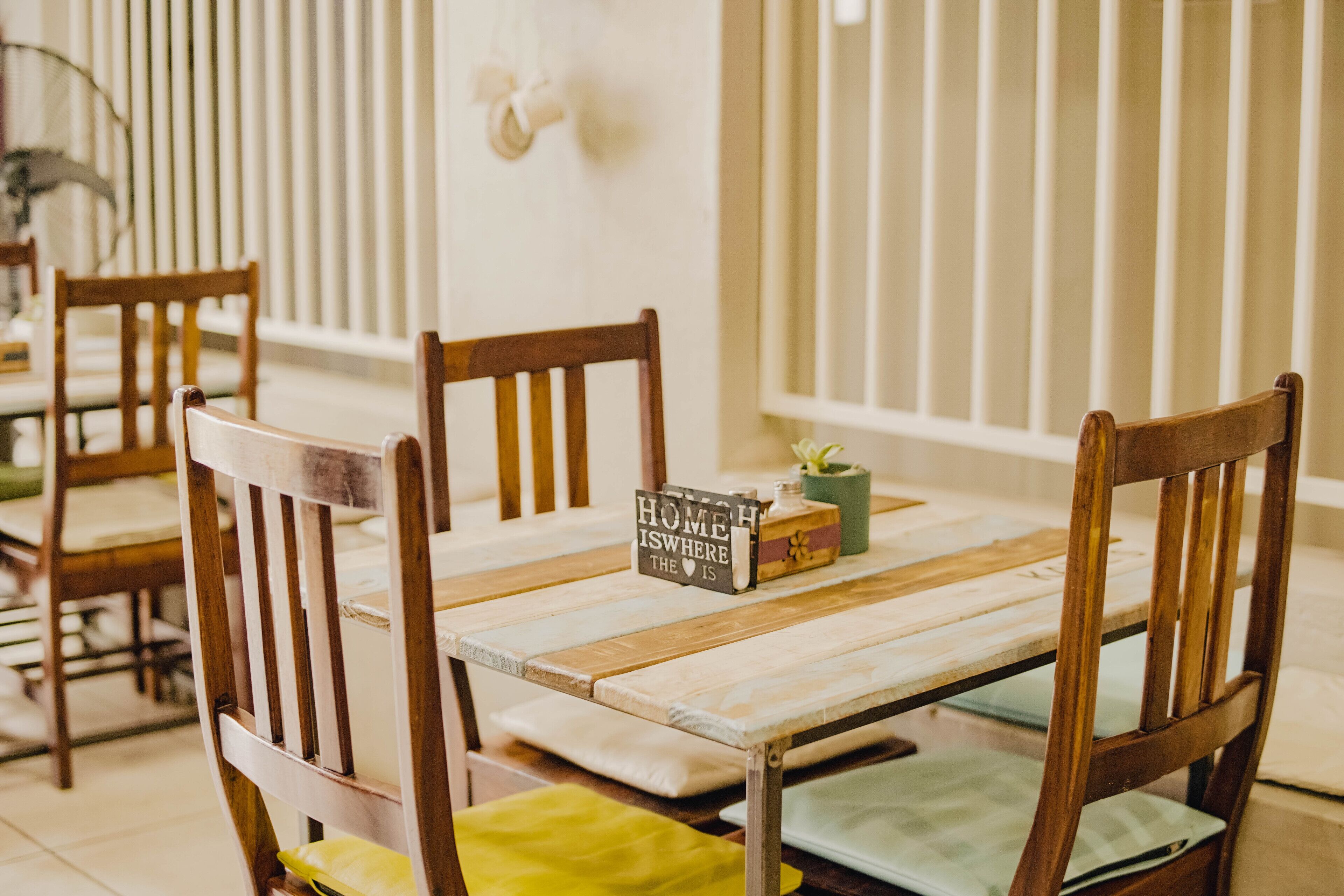 Un comedor con sillas de madera y una mesa, un libro titulado "HOME IS WHERE THE HEART IS" y un pequeño jarrón con una planta.
