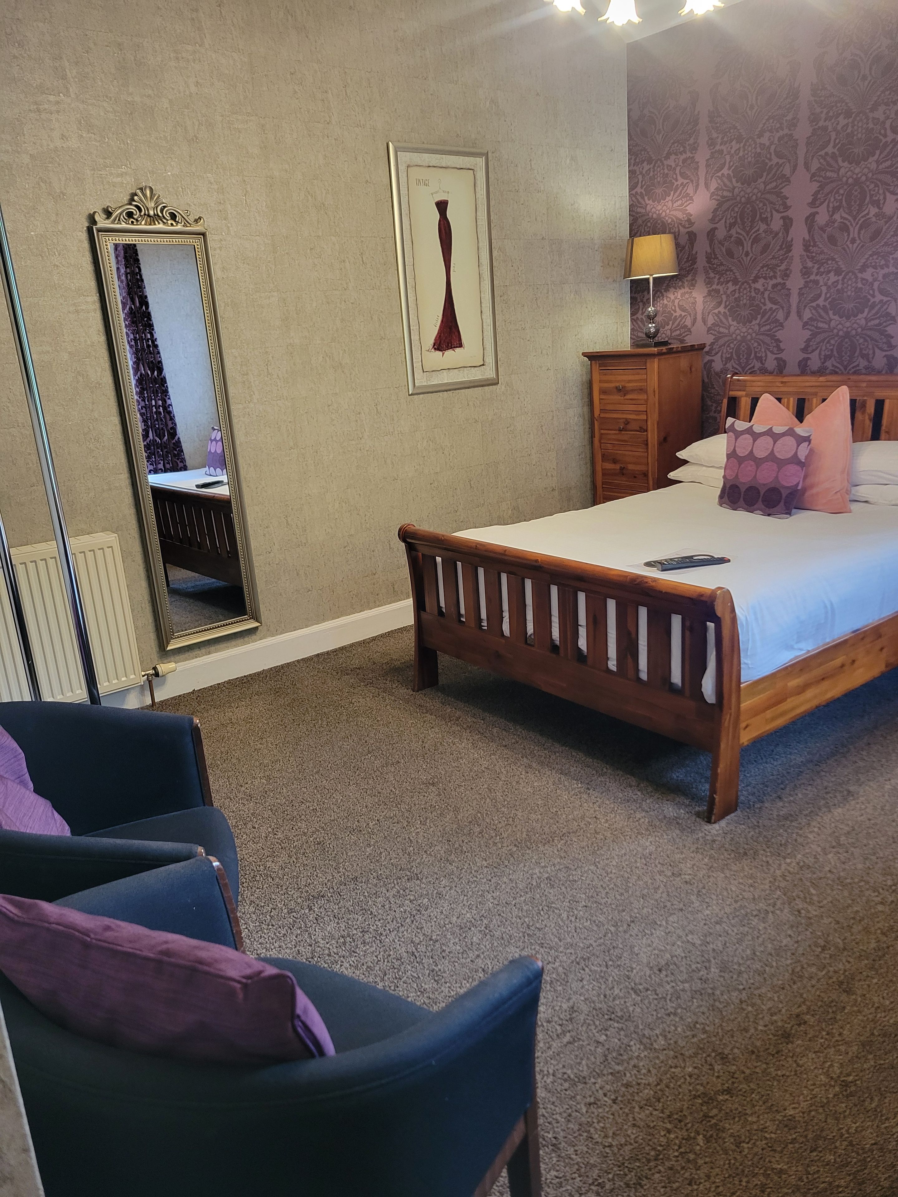 A bedroom with a bed, a chair, a dresser, a mirror, and a wall with a floral pattern.