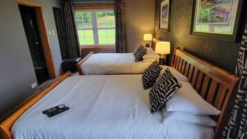A double bed with a remote control, two bedside lamps, patterned pillows, and a view of a garden through a window.