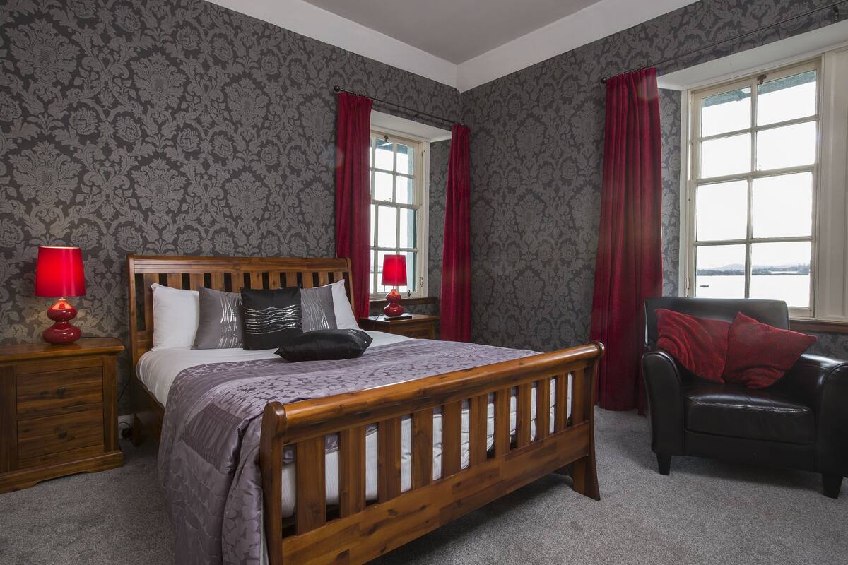 A bedroom with a wooden bed, two nightstands with lamps, a chair, and a window with curtains.