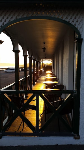 A covered outdoor seating area with tables and chairs, a view of the sunset, and a parking lot in the background.