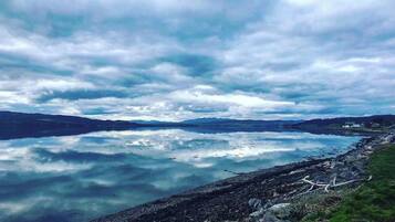 Un llac tranquil amb riba rocosa i muntanyes llunyanes sota un cel nuvolós.