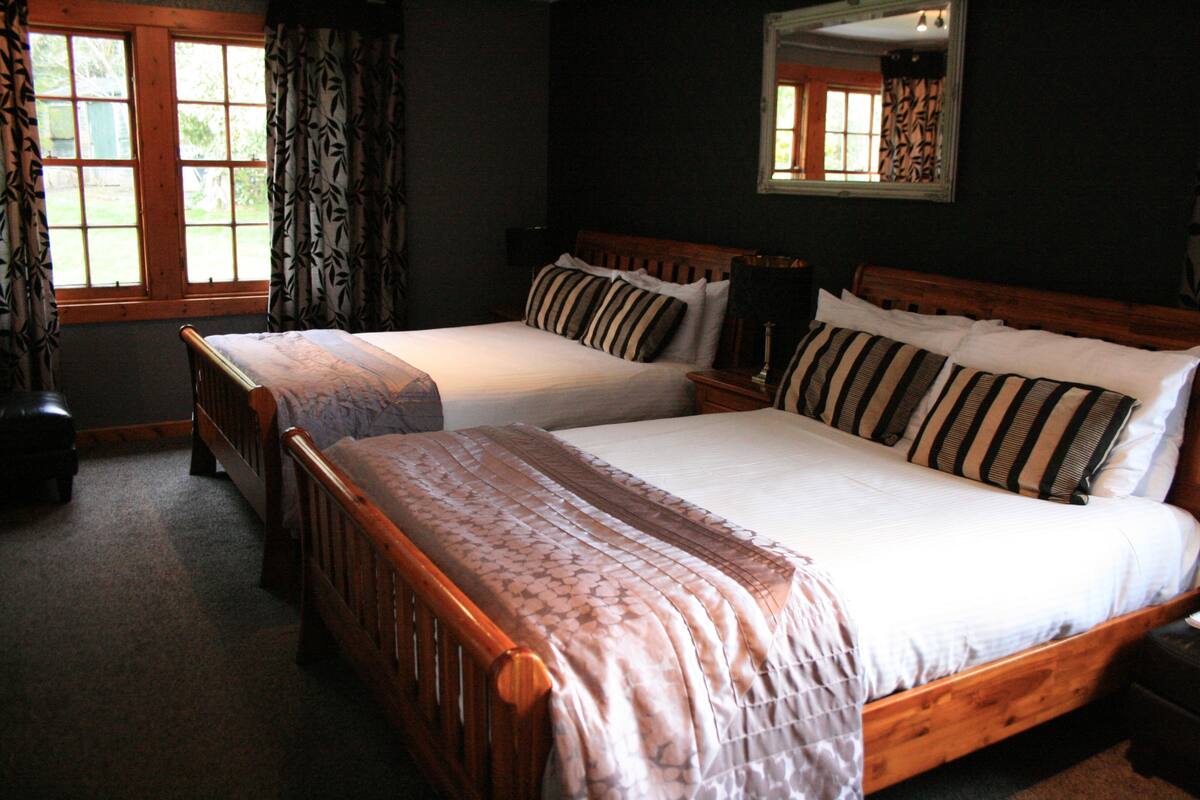 A double bed with a wooden frame and a floral bedspread, a nightstand with a lamp, and a window with curtains.