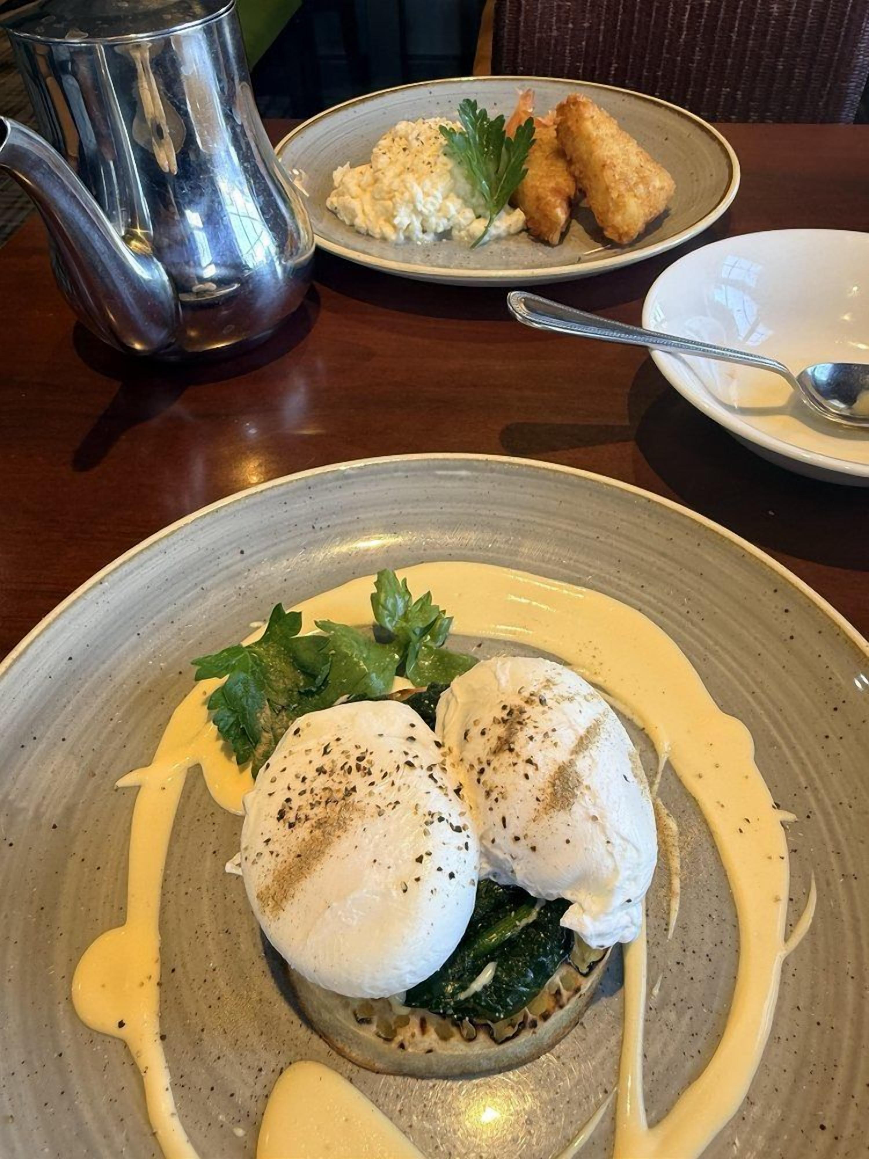 Une table à manger avec une assiette de nourriture, une théière en argent et une cuillère.