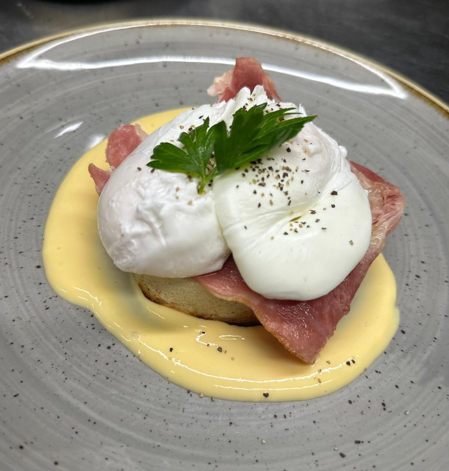 Un plato con huevos pochados, prosciutto y salsa holandesa.