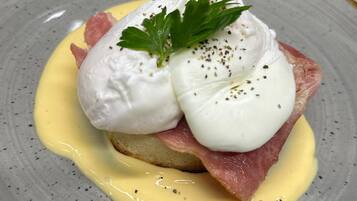 Un plato con huevos pochados, prosciutto y salsa holandesa.