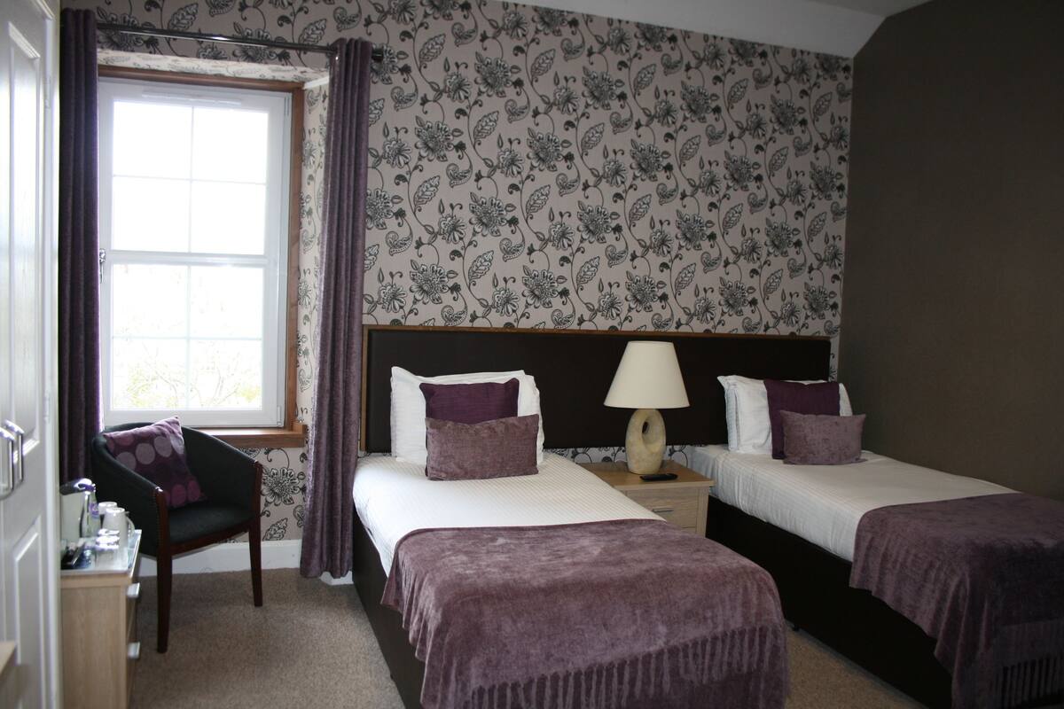 A hotel room with two beds, a chair, a desk, and a window with curtains.