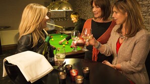 Un gruppo di persone a un tavolo da biliardo, con una bottiglia di vino e dei bicchieri.