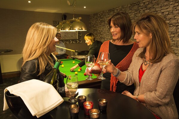 A group of people at a pool table with a bottle of wine and glasses on the table. - North Kessock Hotel (Inverness)
