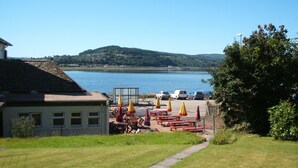 Vista sul lago con tavoli da picnic e ombrelloni, un'area parcheggio e un edificio con tetto spiovente.