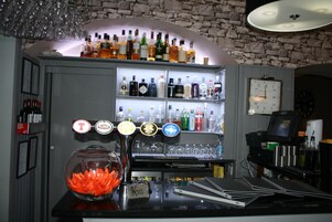 Zona de bar con estantes llenos de botellas de licores, un pecera y un reloj en la pared.