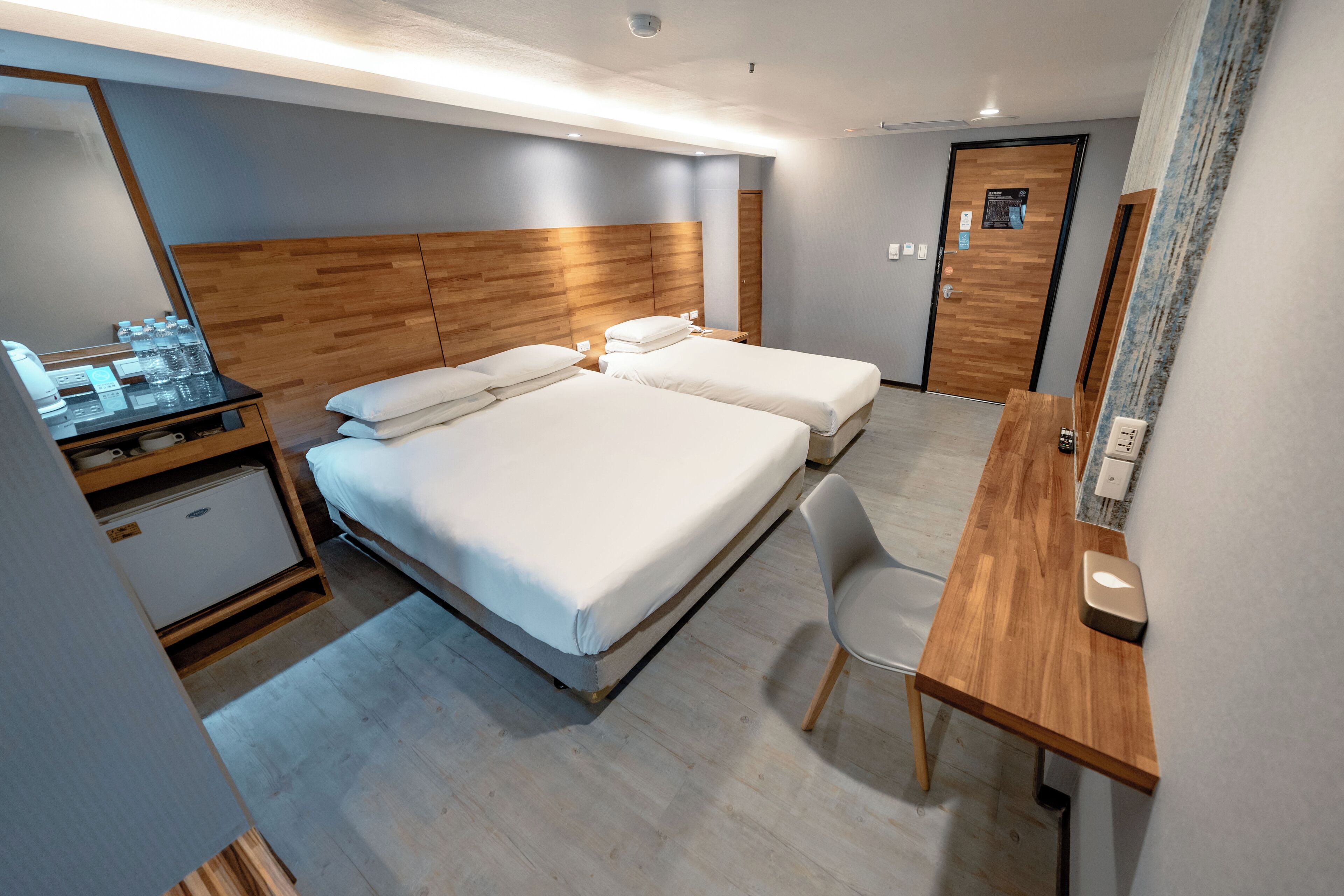 A hotel room with two beds, a wooden desk, a chair, a minibar, and a mirror.