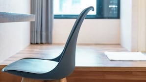 A modern chair with wooden legs and a curved backrest, positioned in front of a window with a view of the city. - Hotel Cloud Arena-Daan (Taipei)