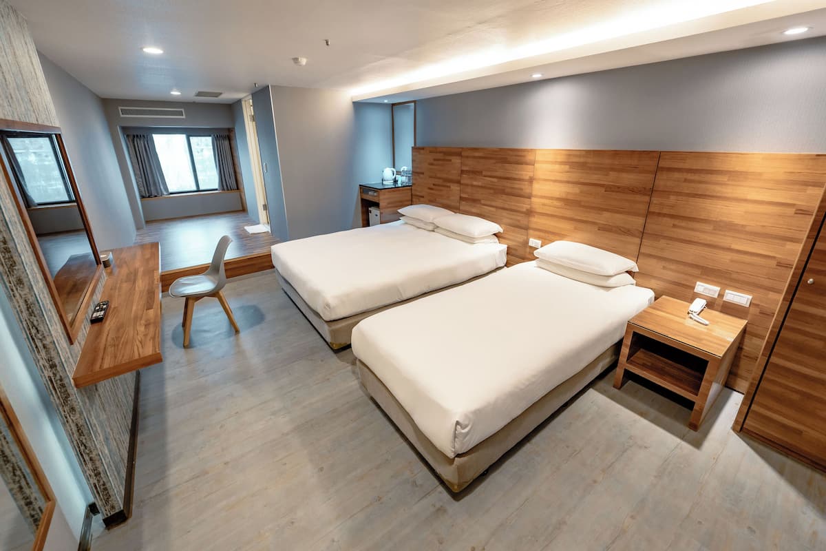 A modern hotel room with two beds, a desk, and a chair.