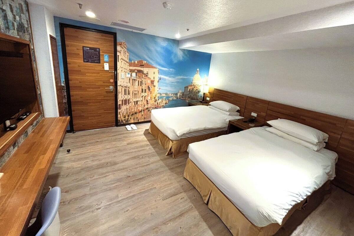 A hotel room with two beds, a desk, and a TV.