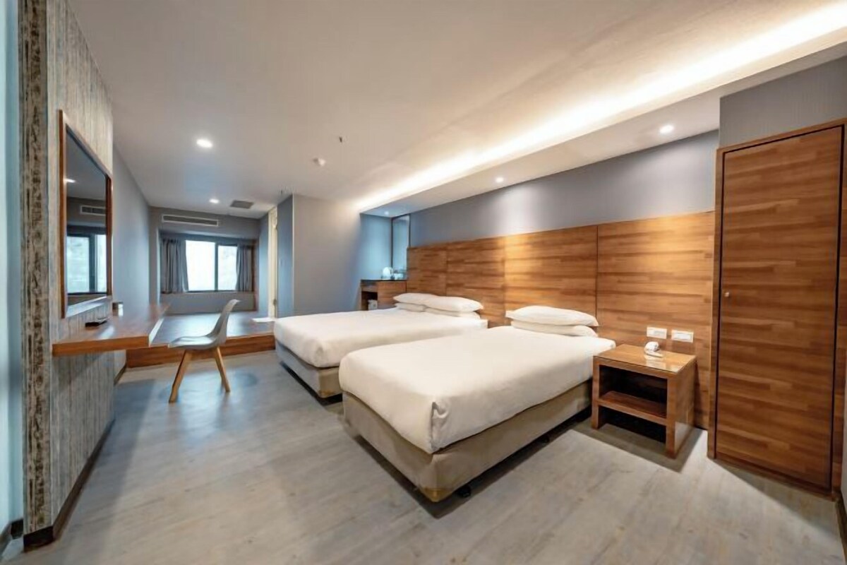 A modern hotel room with two beds, a desk, and a chair.