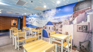 A restaurant with wooden tables and chairs, a mural of a coastal town, and a blue ceiling. - Hotel Cloud Arena-Daan (Taipei)