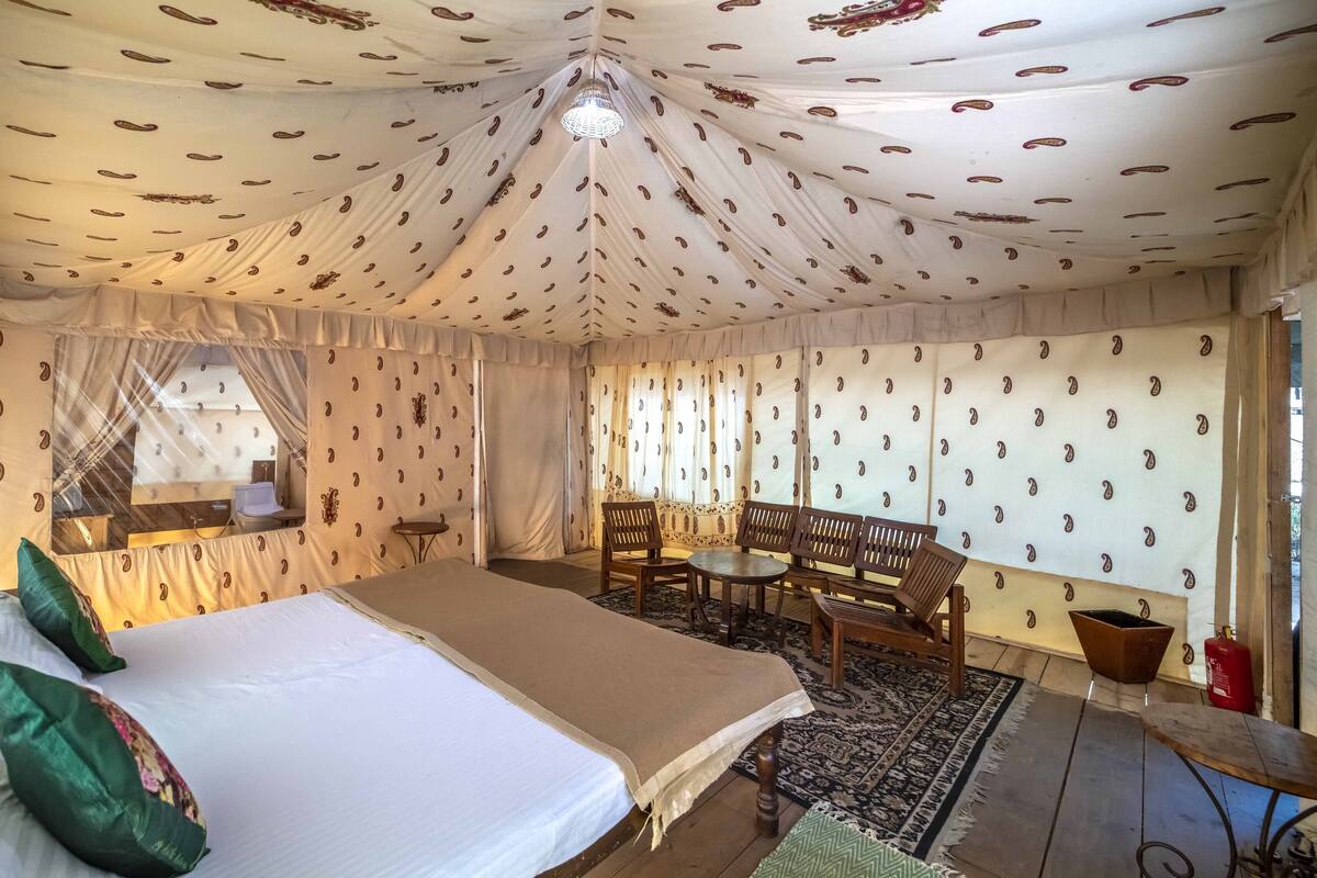 Une pièce aménagée comme une tente, avec un lit, une table et des chaises, un miroir et des murs décorés de motifs.