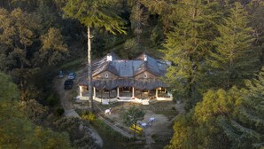 Una casa gran i rústica envoltada de bosc dens, amb carrer d'accés pavimentat i zona d'estar a l'aire lliure.