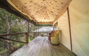 A covered wooden deck with a table and chairs, surrounded by trees.