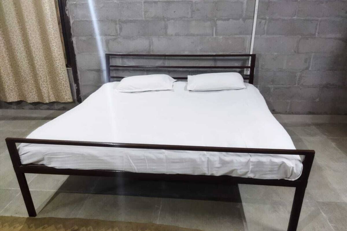 Un lit avec un matelas blanc et deux oreillers, placé contre un mur de briques et sur un tapis à motifs.
