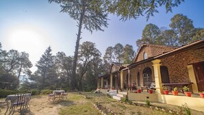 Edifici rústic amb façana de maó, un porxo amb plantes en testos i una zona de menjador amb taules i cadires.