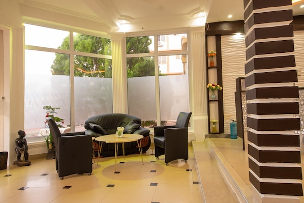 Una sala de estar moderna con un sofá de cuero negro, una mesa redonda y sillones negros. Amplias ventanas ofrecen vistas a zonas verdes.