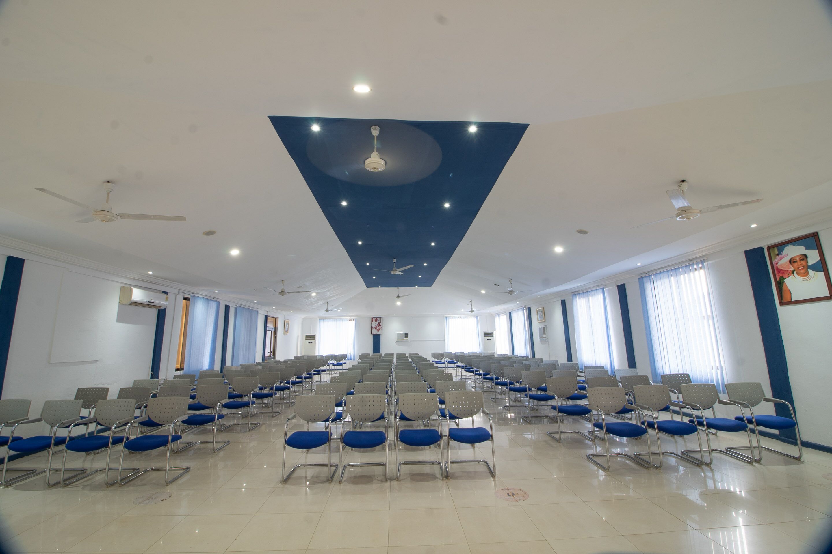 A spacious hall with rows of chairs and ceiling fans, large windows, and a blue accent wall.