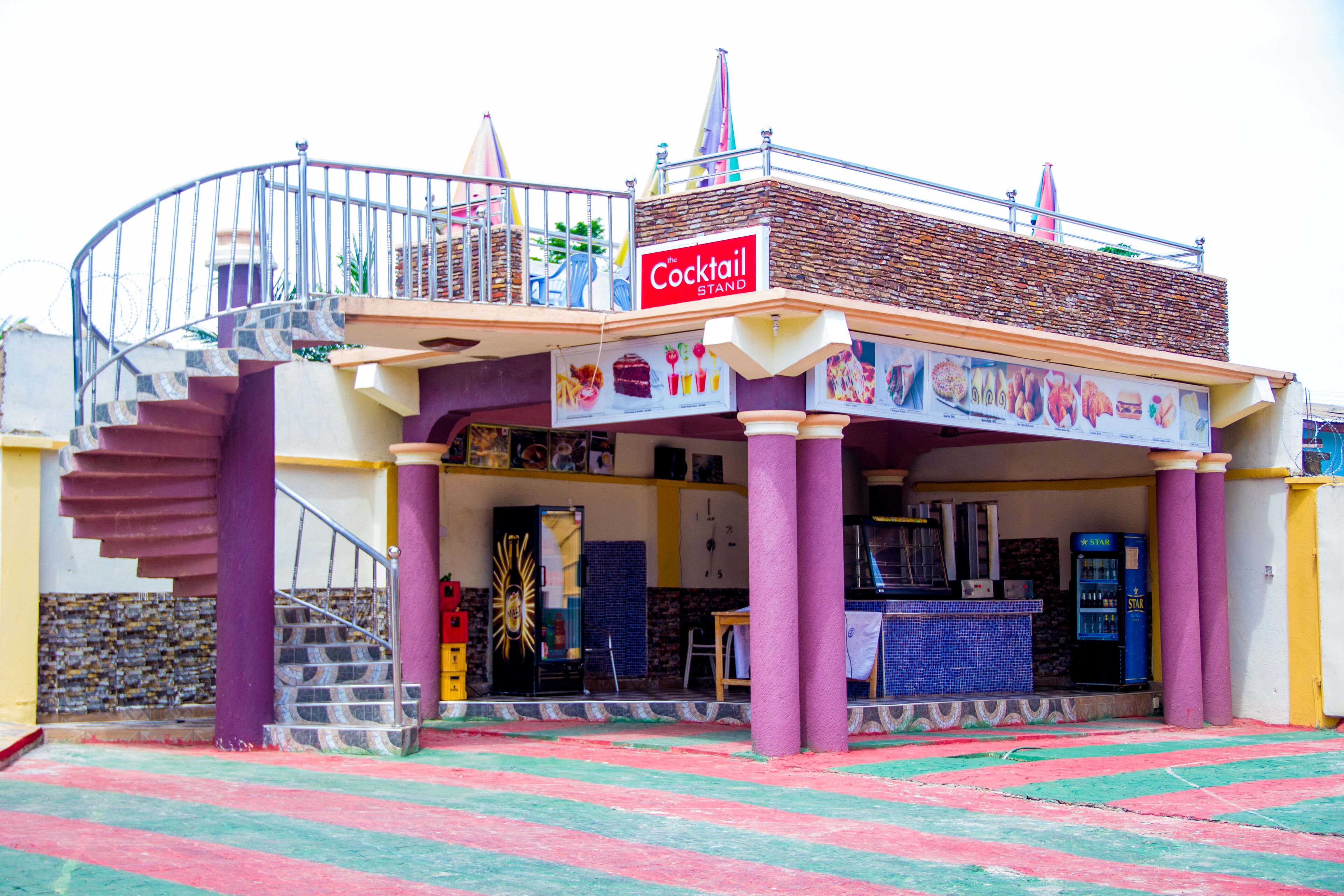 Un bâtiment sur lequel on peut lire l’inscription « Cocktail Stand », avec un escalier, un comptoir et une machine à café Starbucks.