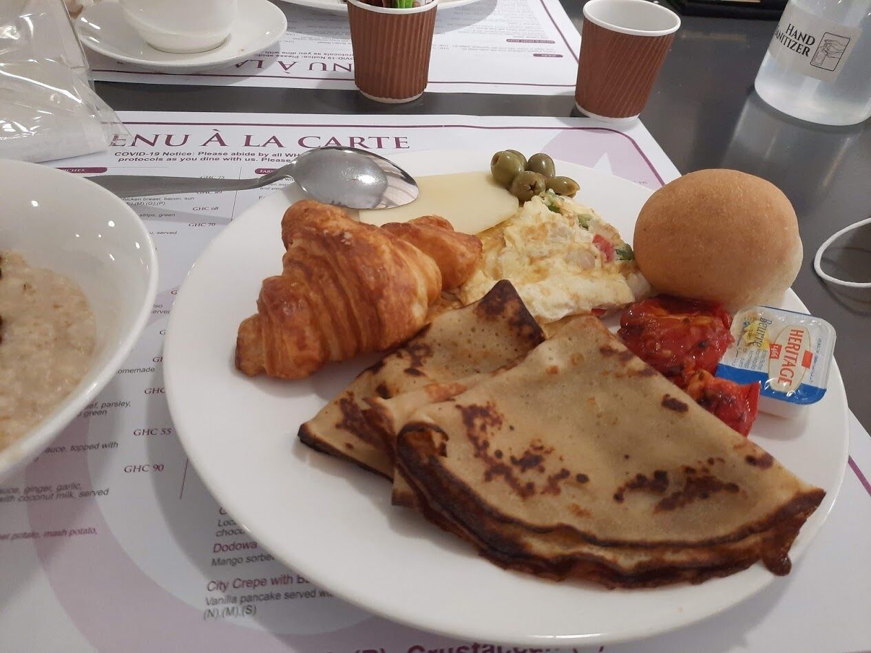 A breakfast plate with croissants, pancakes, and a small container of yogurt.