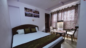 A hotel room with a bed, a desk, and two chairs. There are four pictures on the wall. - Hotel Mohit Palace (Jaipur)