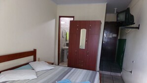 Un dormitorio con cama, armario de madera, televisión y baño visible a través de una puerta abierta.