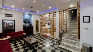 A hotel lobby with a checkered floor, a red sofa, a wooden partition with framed pictures, and a staircase. - Janak Niwas (Udaipur)