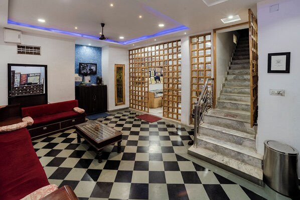 Un vestíbulo de hotel con piso a cuadros, un sofá rojo, una división de madera con cuadros enmarcados y una escalera.