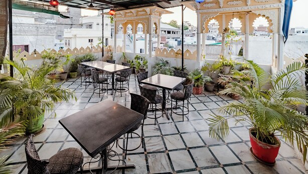 An outdoor seating area with tables and chairs, surrounded by potted plants. - Janak Niwas (Udaipur)