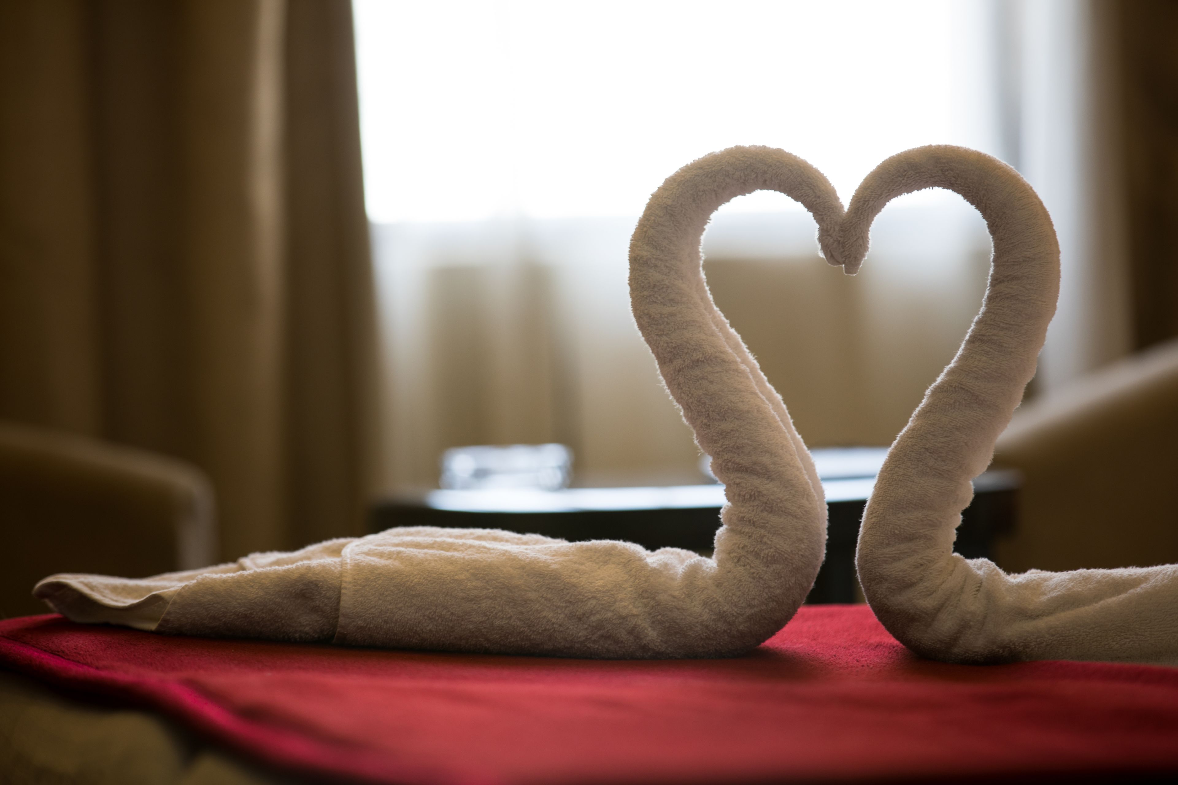 A bed with a red blanket and two swan-shaped towels arranged on it.