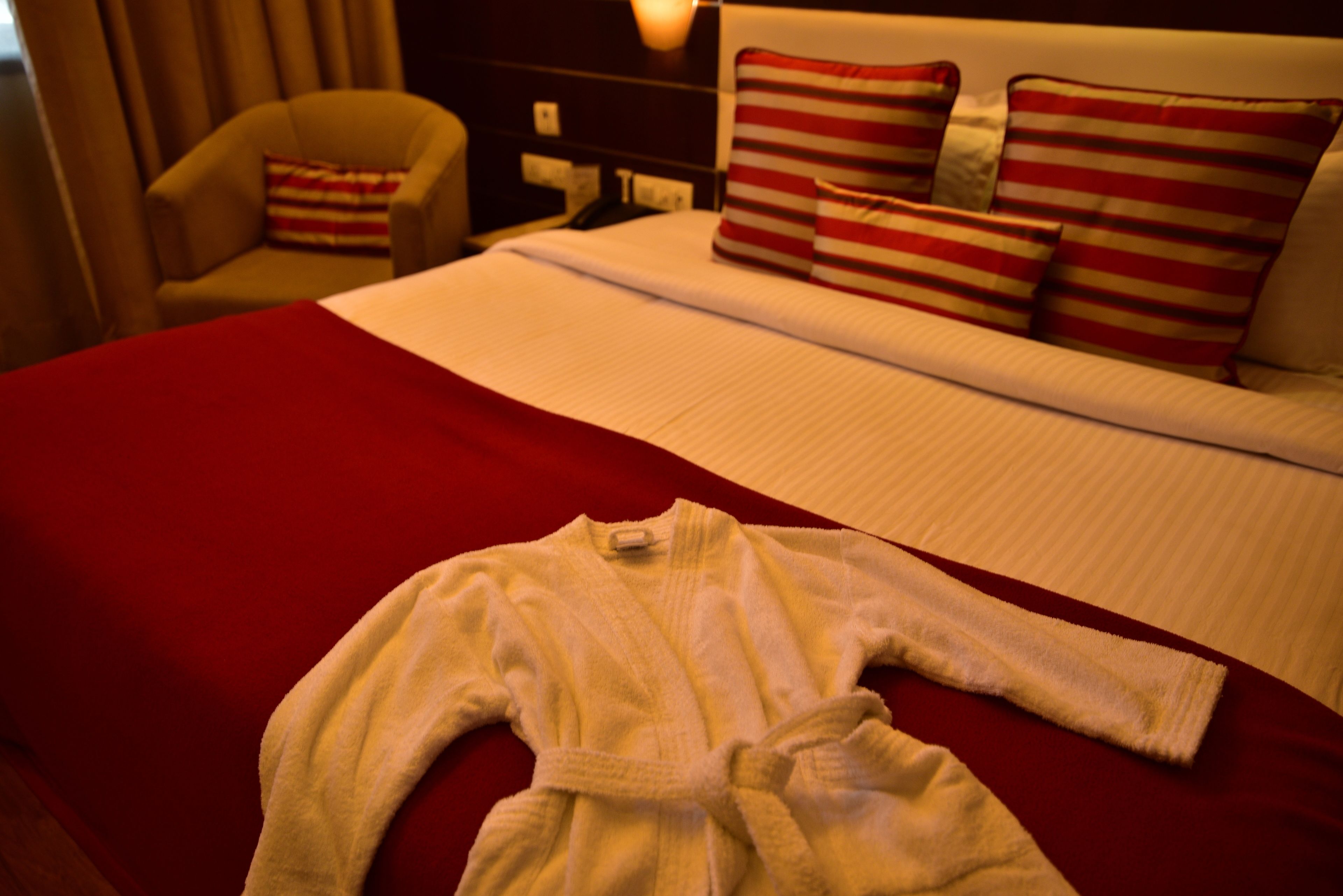 Un letto rifatto con un copriletto rosso e un accappatoio bianco.