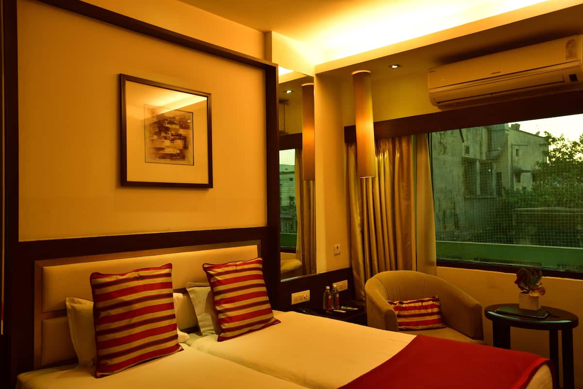 A hotel room with a bed, a chair, a nightstand, and a window with curtains.