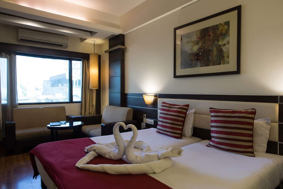 A hotel room with a bed, a sofa, a small table, a lamp, and a painting on the wall.