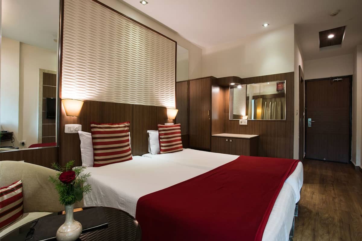 A hotel room with a large bed, bedside tables, a mirror, a vanity, and a door.