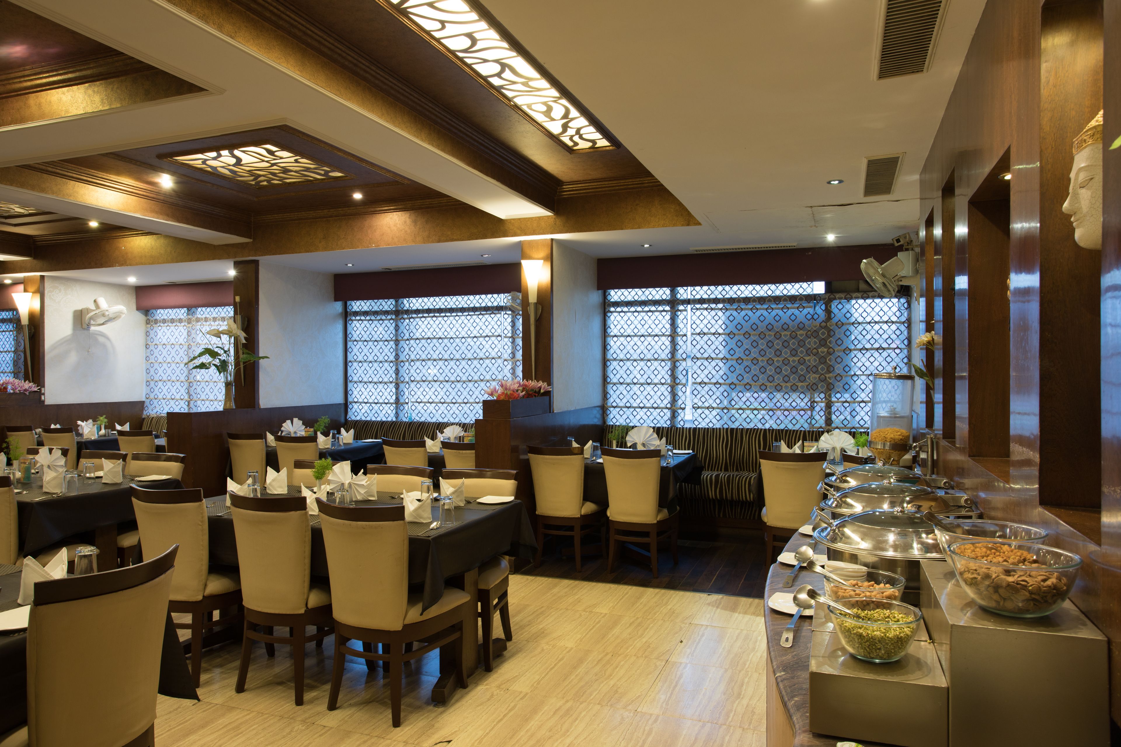 Un ristorante con diversi tavoli e sedie, un'area buffet con vari contenitori per il cibo e elementi decorativi su pareti e soffitto.